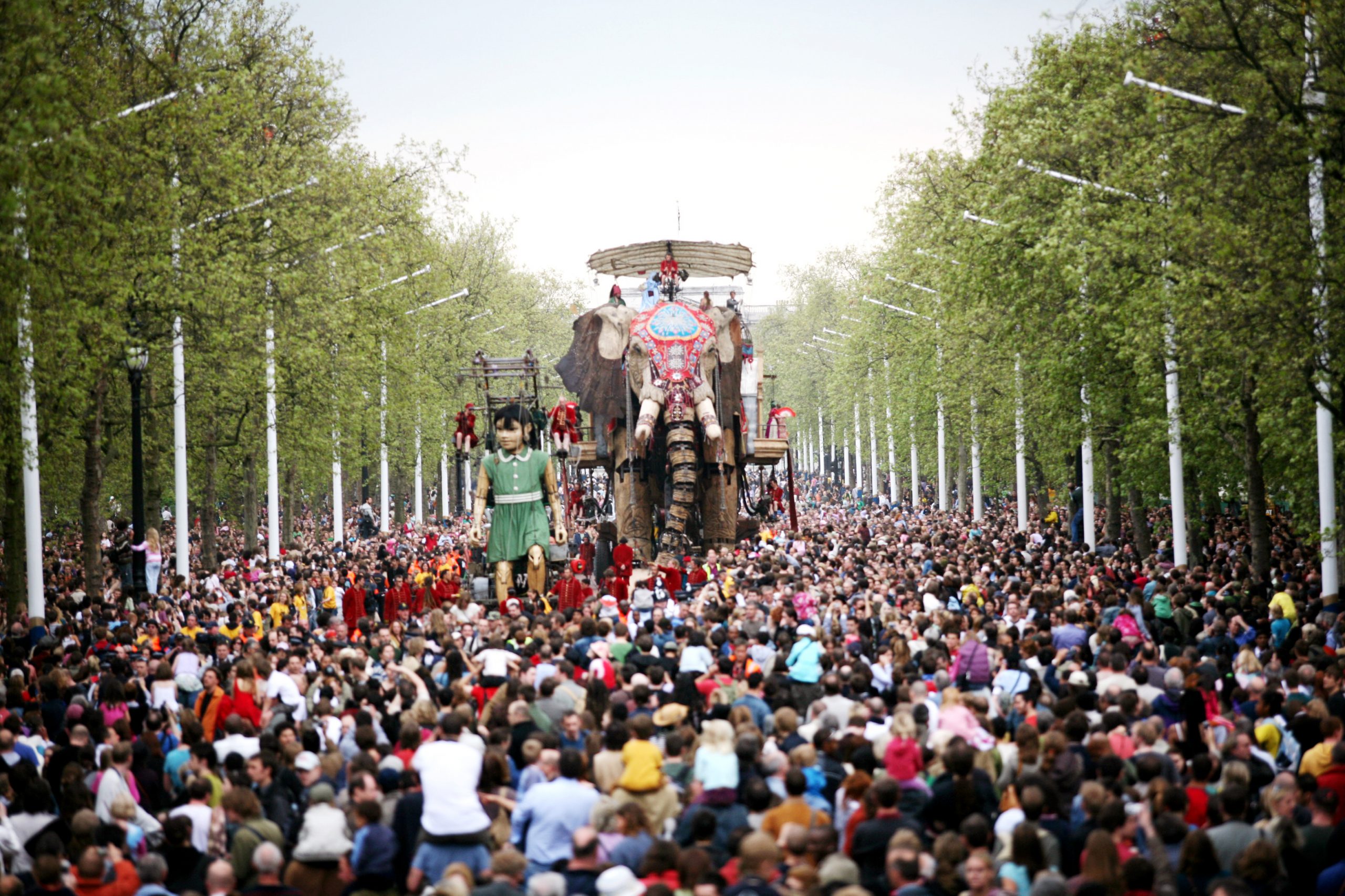 A giant puppet Elephant tin a public street filled with people.