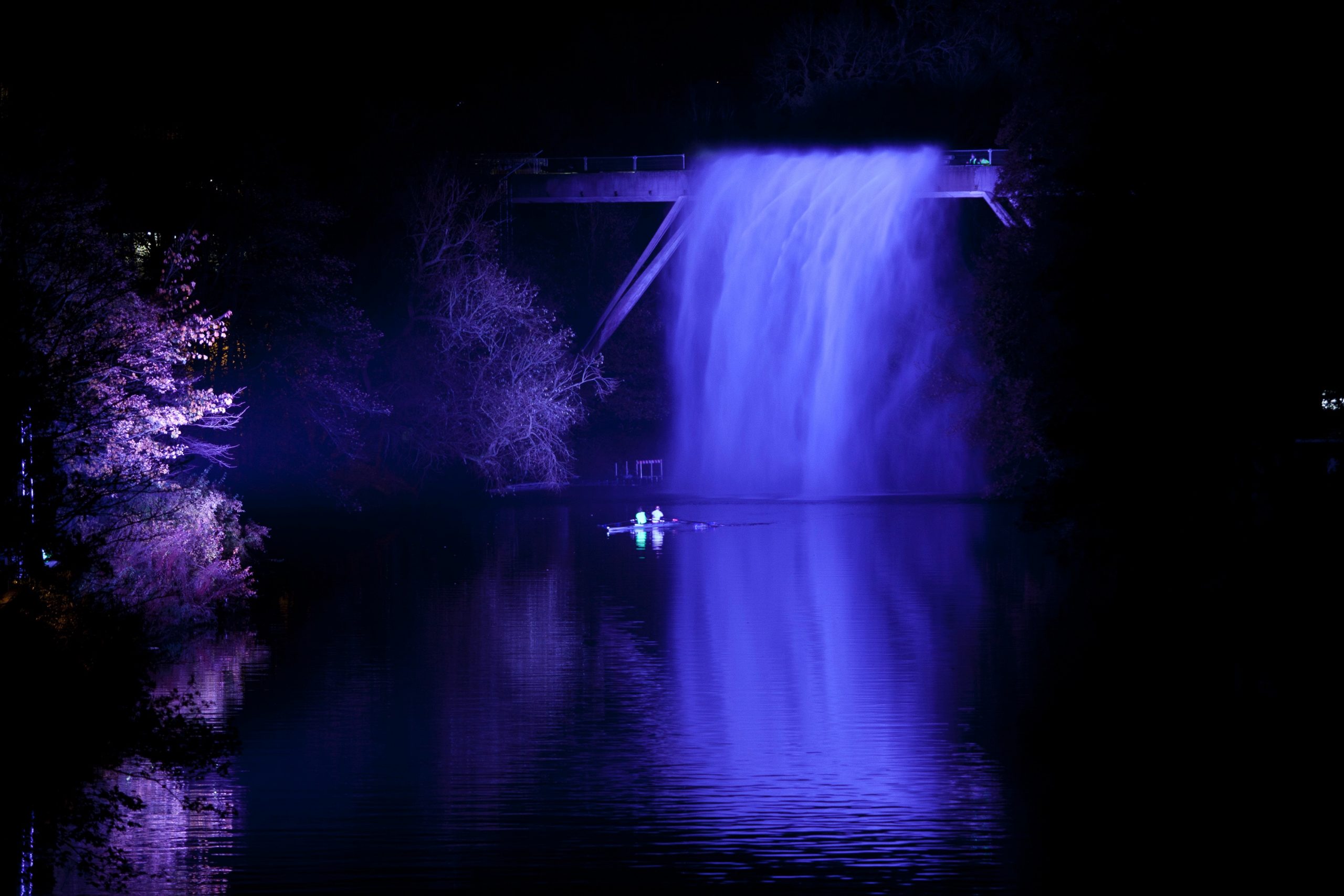 Illuminated purple waterfall with canoes underneath