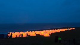 Peace camp at Dunstanburgh Castle, Craster, Northumberland. Behind the glowing tents at dusk is the seafront