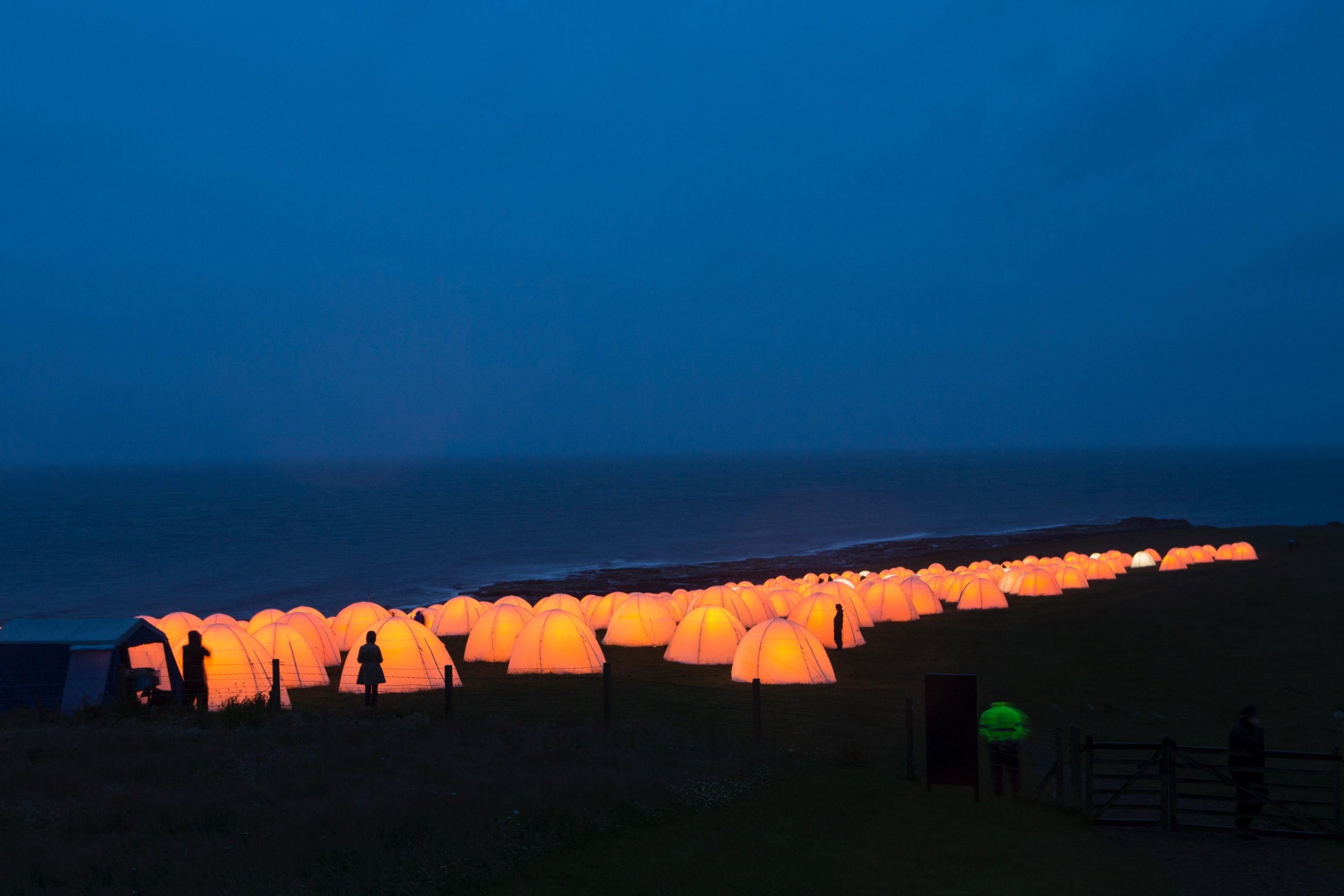 Peace camp at Dunstanburgh Castle, Craster, Northumberland. Behind the glowing tents at dusk is the seafront