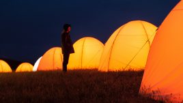 Boy standing in front of glowing tent in the dark