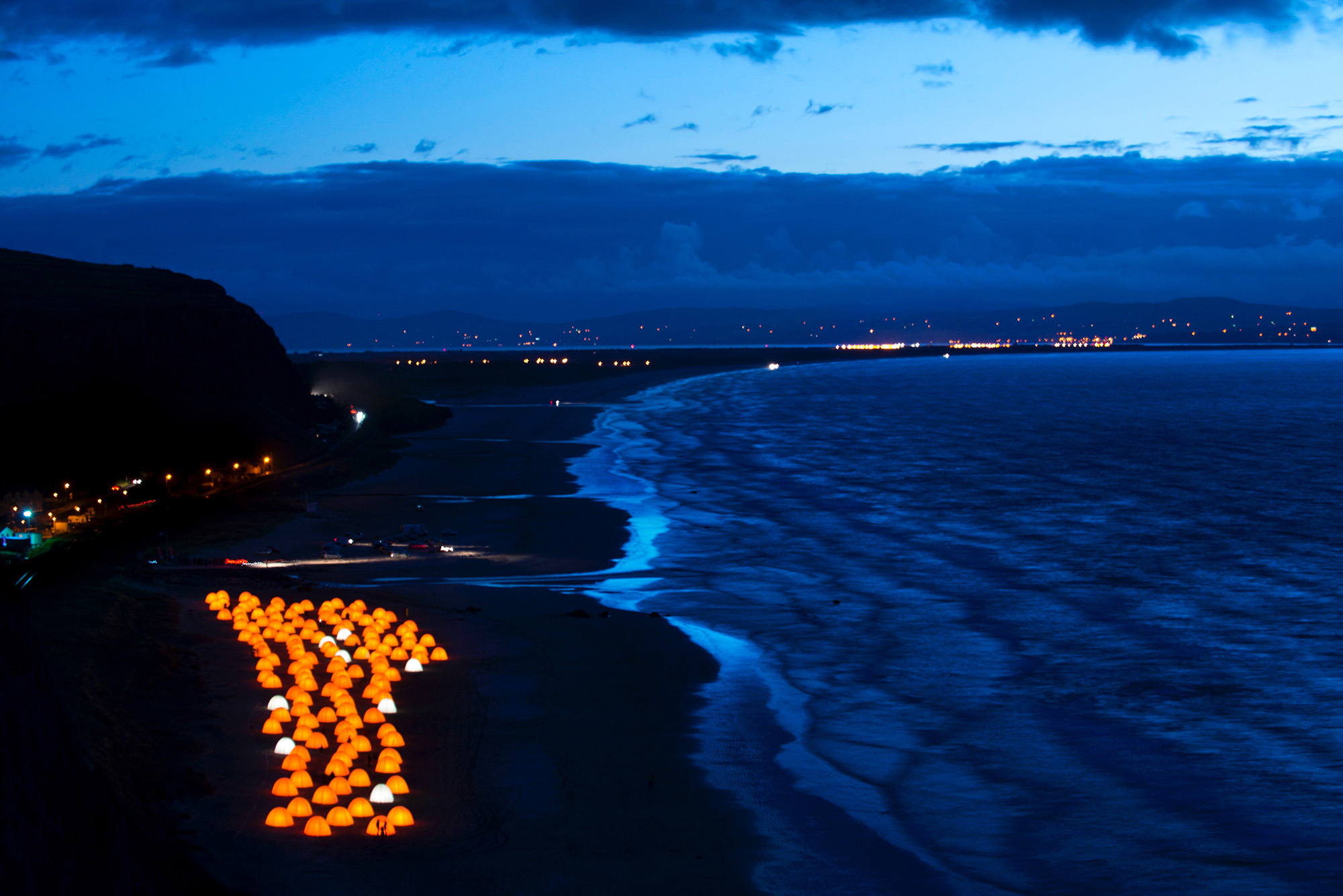 Aerial shot of peace camp tents glowing at dusk by the seafront