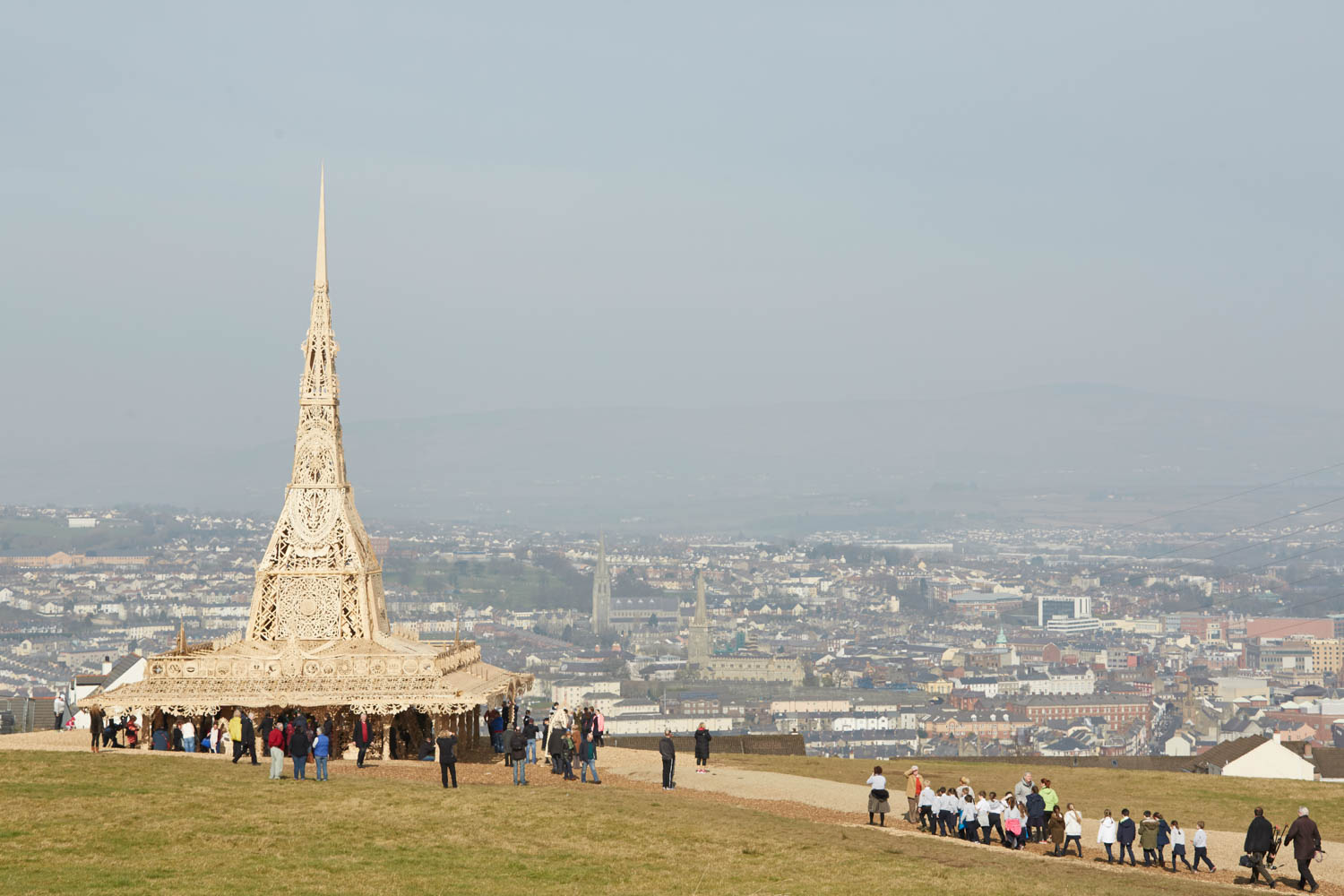 View of the people walking around Temple in the day on a hill with Derry~Londonderry visible in the background