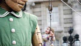 A giant puppet of a little girl wearing a green dress.