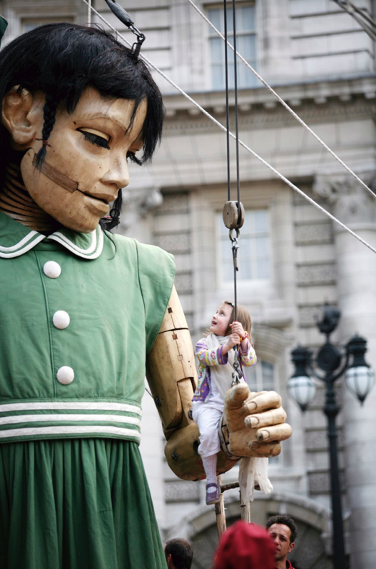 A giant puppet of a little girl wearing a green dress.