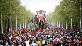 A giant puppet Elephant tin a public street filled with people.