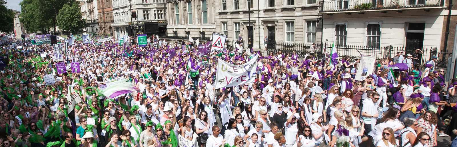 Crowd of women dressed in purple, white and green holding up banners