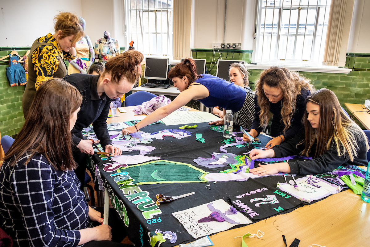 Women sitting around a table collaboratively crafting and sewing a banner.