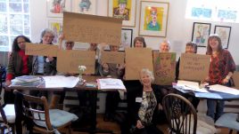 Ten women are standing holding cardboard squares with empowering slogans written on them like 