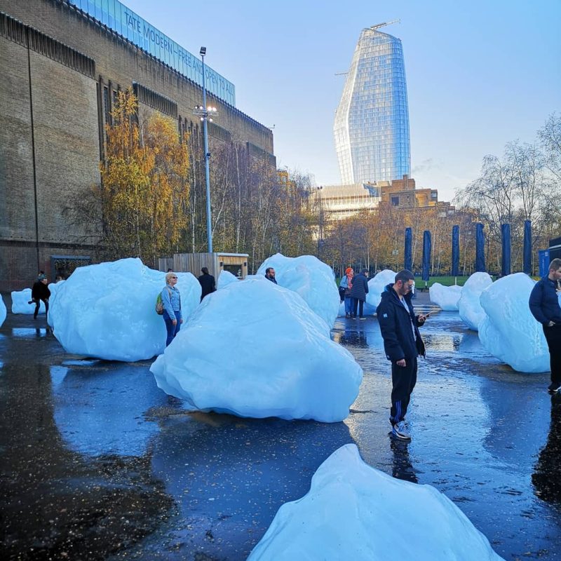 Blocks of ice outside Tate Modern. A man stands next to one chunk of ice looking at his phone.