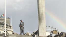 Man standing atop the plinth with a rainbow in the background