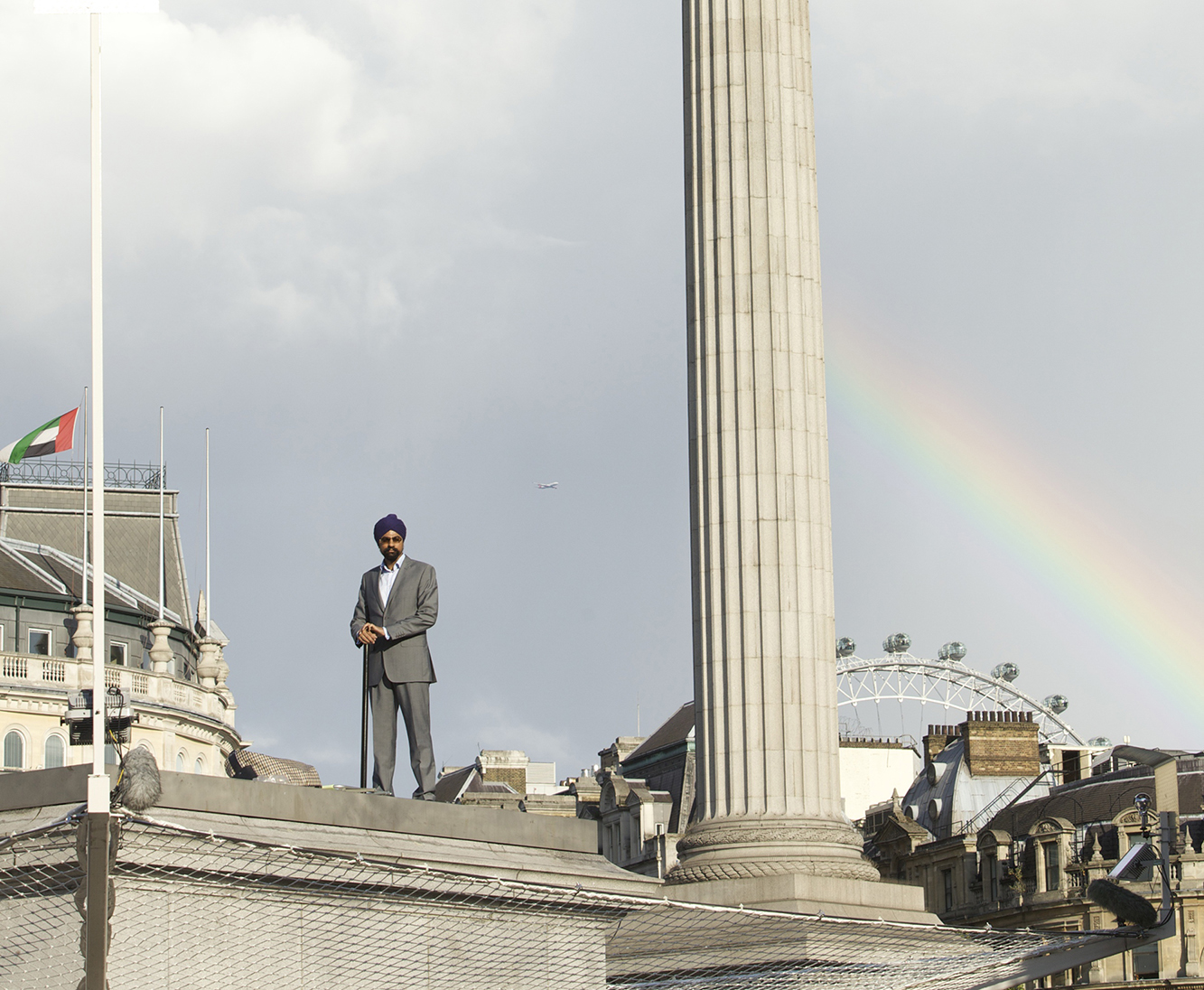 Man standing atop the plinth with a rainbow in the background
