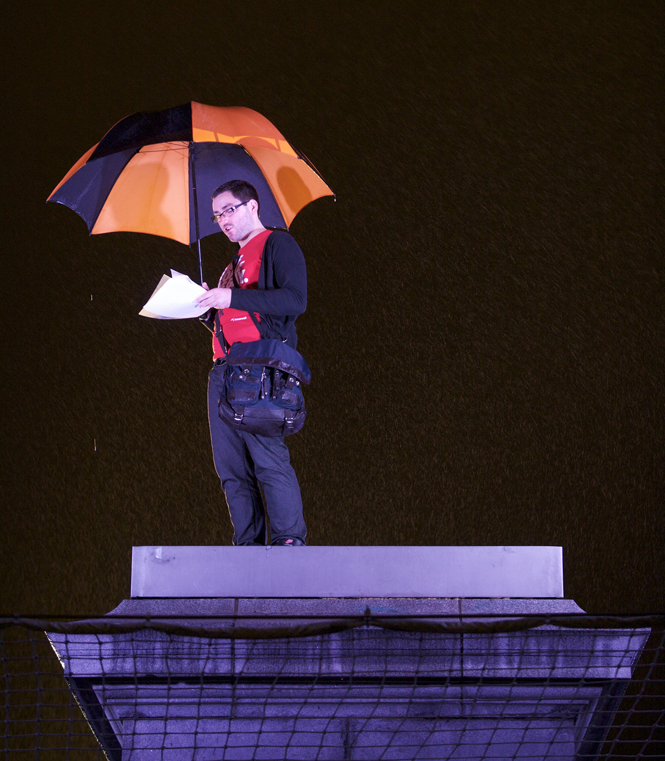 Man standing on the Fourth Plinth at night with umbrella 