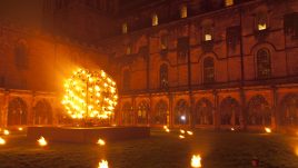 A metal ball with flames surrounded by smaller flames on the ground outside Durham Cathedral