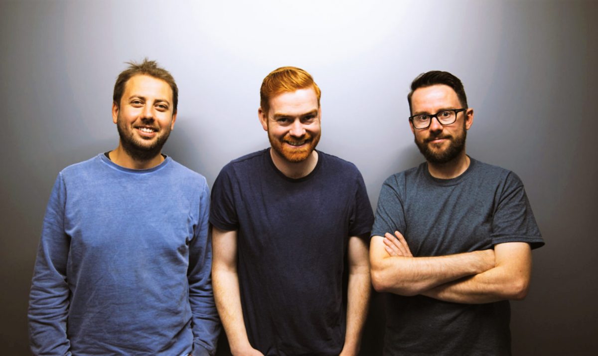 Three men standing against a grey background