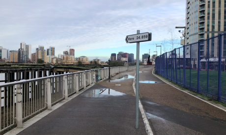 A walkway by the River Thames with a traffic sign planted in the middle, the sign is pointed in the direction of the river on it is written