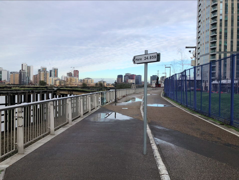 A walkway by the River Thames with a traffic sign planted in the middle, the sign is pointed in the direction of the river on it is written 