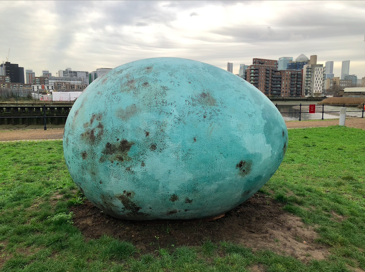 Lying on the grass, a giant egg that is a rusted turquoise colour