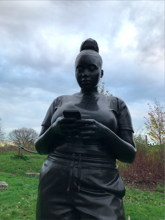 Close up shot of the bronze sculpture, a black woman looking down at her phone