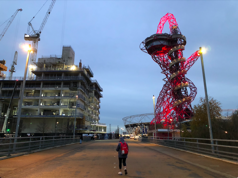 View of the ArcelorMittal Orbit in the evening, with lights shining on it and highlighting the red sculpture, in the shot there is also a building under construction