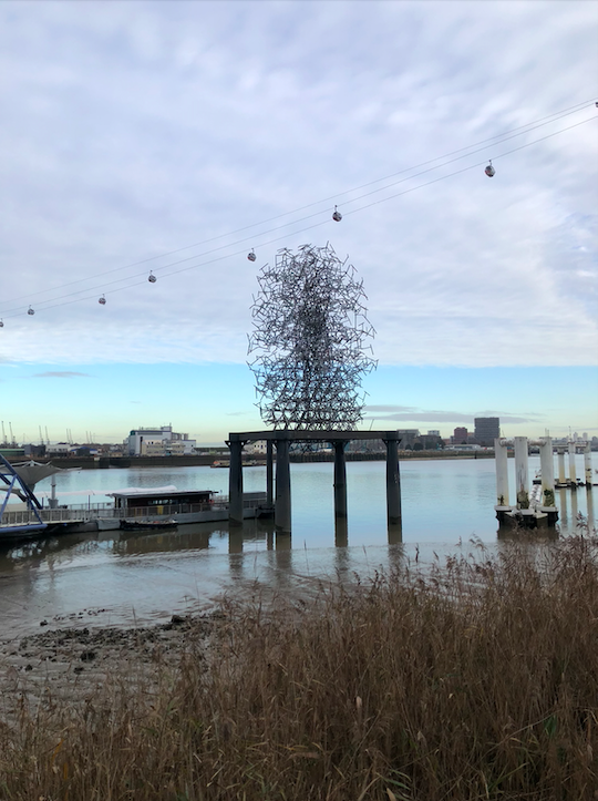 By the pier above the river, the piece is on a plinth which appears like a large table. The sculpture is made of metal and from a distance looks like a ball of energy made from several straight lines coming outwards into the shape of an egg