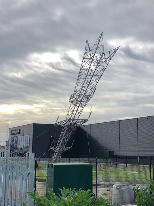 An electricity pylon which is planted into the ground, upside down. It is at a slight 45 degree angle