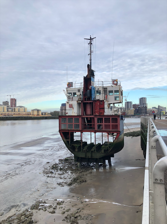 A sliced ocean sand dredger on the river thames. The tide is low so the pillars holding up the ship over the sandy banks are visible