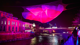 A layered net hung about the River. The net is projected with purple and pink colours.