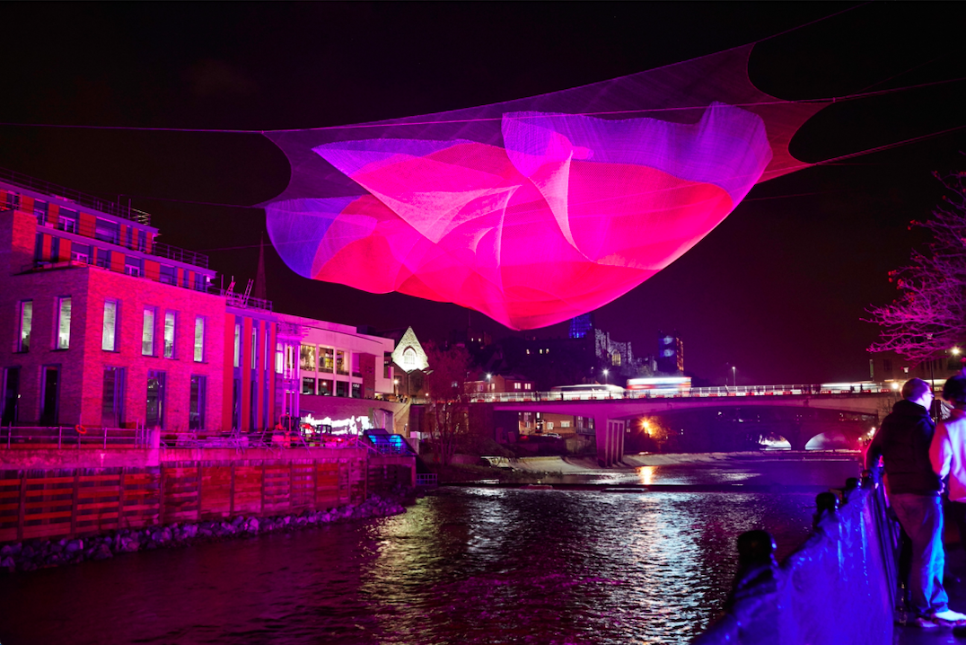 A layered net hung about the River. The net is projected with purple and pink colours.