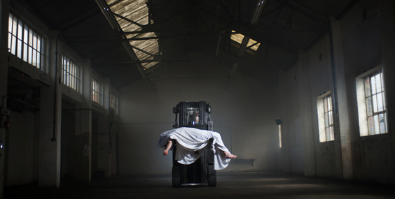 twilightofthefreakingods-large A human figure cloaked in a sheet and suspended from the roof of a warehouse. Stan's Cafe, Twilight of the Freaking Gods
