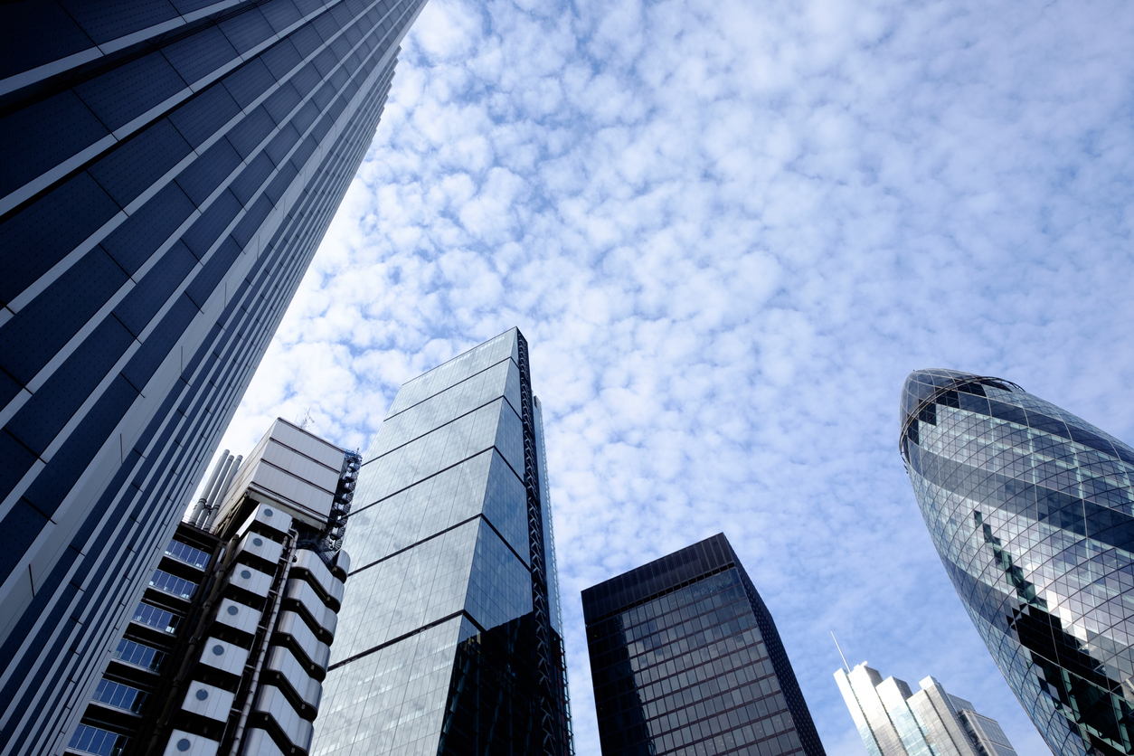 Upward view of sky scrapers office blocks in a central city with blue sky and light cloud behind