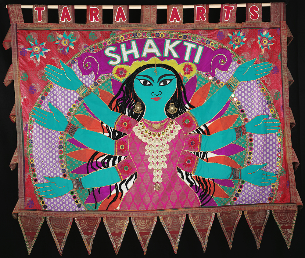 Blue human figure with 6 arms against pink and orange background made from recycled saris.