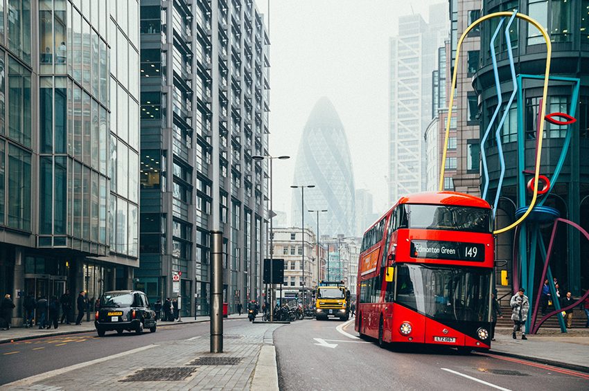 A red London bus passing through a street of skyscrapers in central London