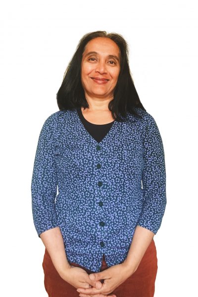 Headshot of Daksha smiling and wearing a blue cardigan, black top and red trousers