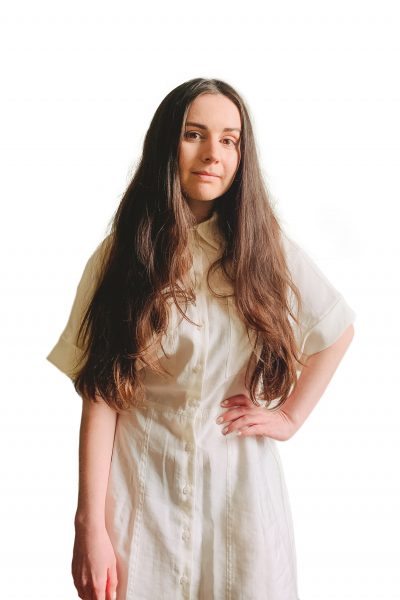 Headshot of Erin, she has one hand on her right hip and is wearing a cream dress