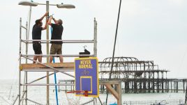 Two men on scaffolding attaching speakers to a lamp post