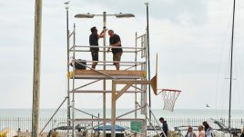 Two men on scaffolding attaching speakers to a lamp post