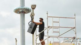 man on scaffolding attaching speakers to a lamp post