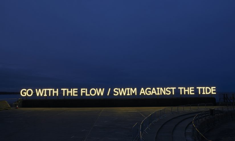 Illuminated text reads: Go with the flow / swim against the tide