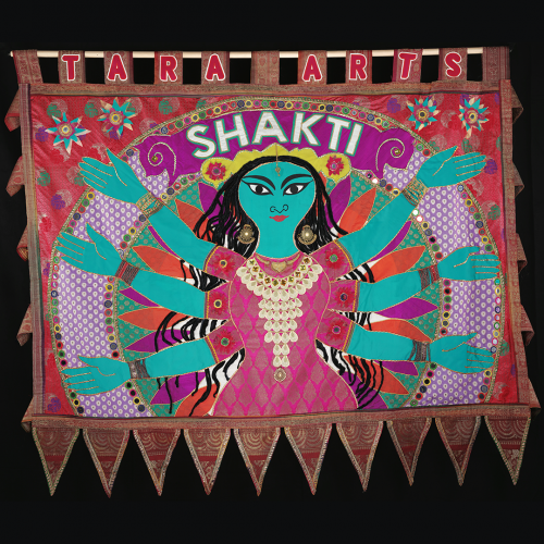 Blue human figure with 6 arms against pink and orange background made from recycled saris. SHAKTI is written above its head.