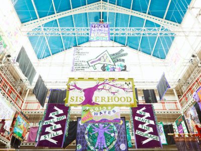 Below view of colourful banners with different messages around women's rights hanging in a brightly lit building