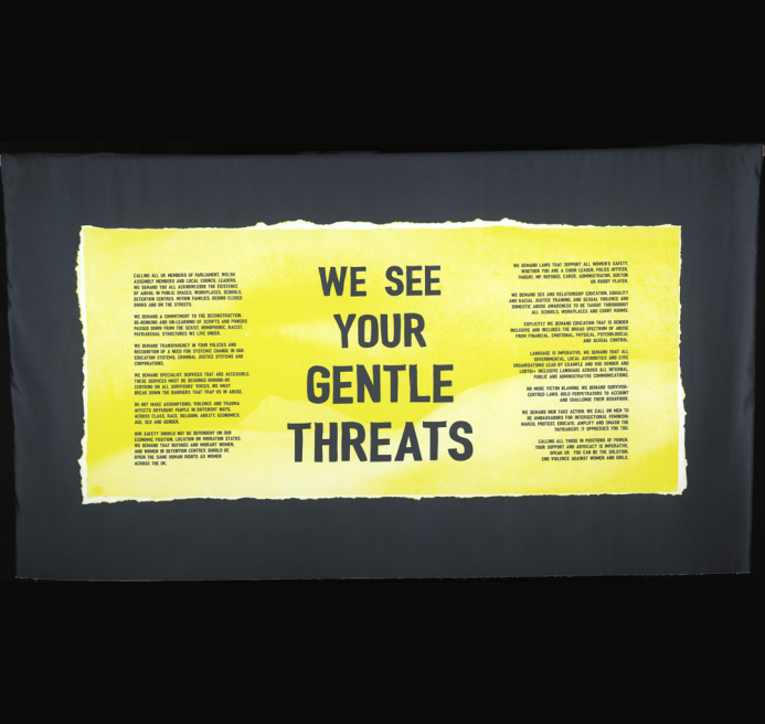 A yellow banner, at the centre are the words “WE SEE YOUR GENTLE THREATS” On the banner is also the manifesto collectively writen by a group of women from South Wales who have encountered gender-based violence.