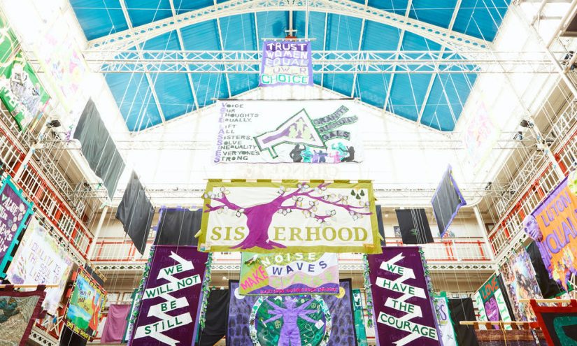 Below view of colourful banners with different messages around women's rights hanging in a brightly lit building