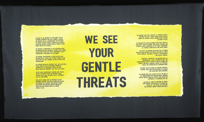 A yellow banner, at the centre are the words “WE SEE YOUR GENTLE THREATS” On the banner is also the manifesto collectively writen by a group of women from South Wales who have encountered gender-based violence.
