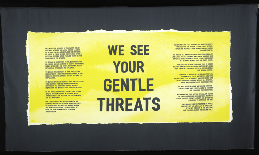 Banner by HEXXX working with Welsh Women’s Aid A yellow banner, at the centre are the words “WE SEE YOUR GENTLE THREATS” On the banner is also the manifesto collectively writen by a group of women from South Wales who have encountered gender-based violence.