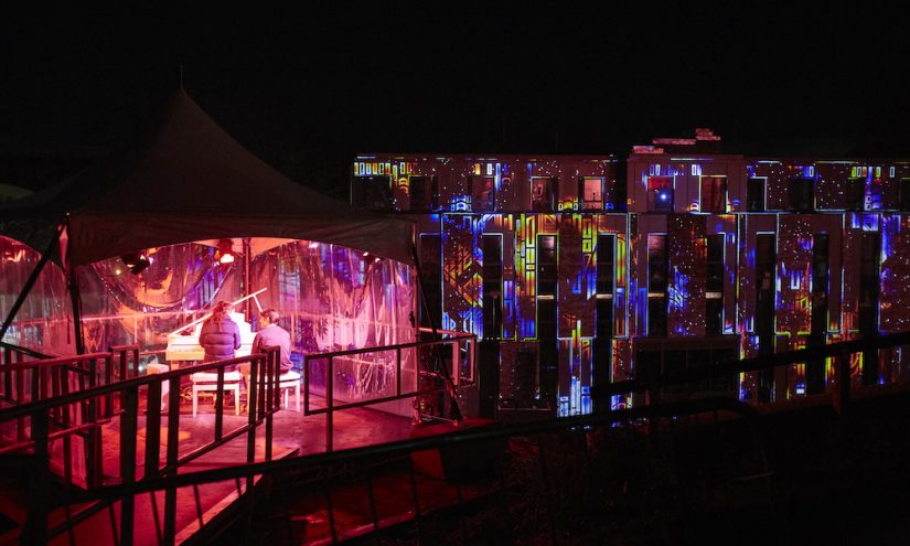 Participants playing the piano to create a light multicoloured light projection on the building in front of them