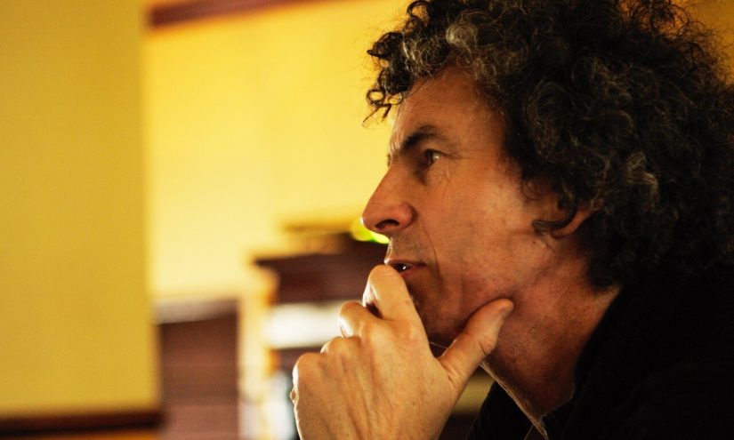 A profile photo of composer Orlando Gough. He has dark curly hair and appears to be deep in thought