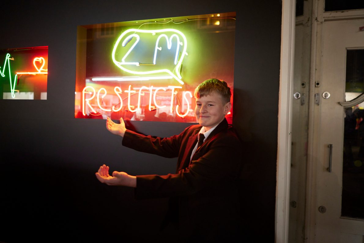 Year 10 student showing his neon artwork which says 