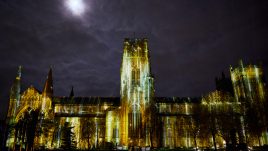Durham Cathedral lit up with a golden rain light projection and a full moon behind the cathedral