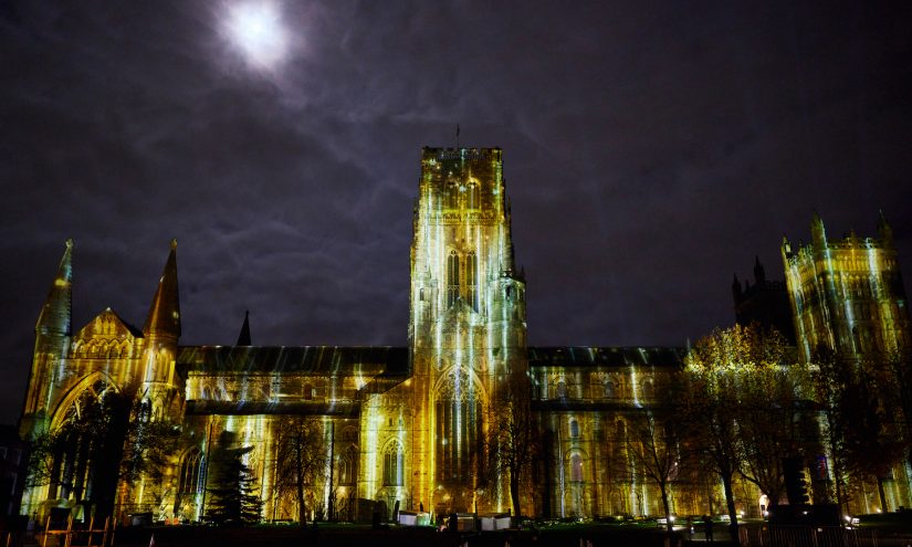Durham Cathedral lit up with a golden rain light projection and a full moon behind the cathedral